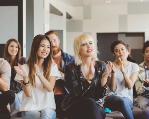 Large group of happy multi ethnic students attending a seminar at the university, clapping hands.