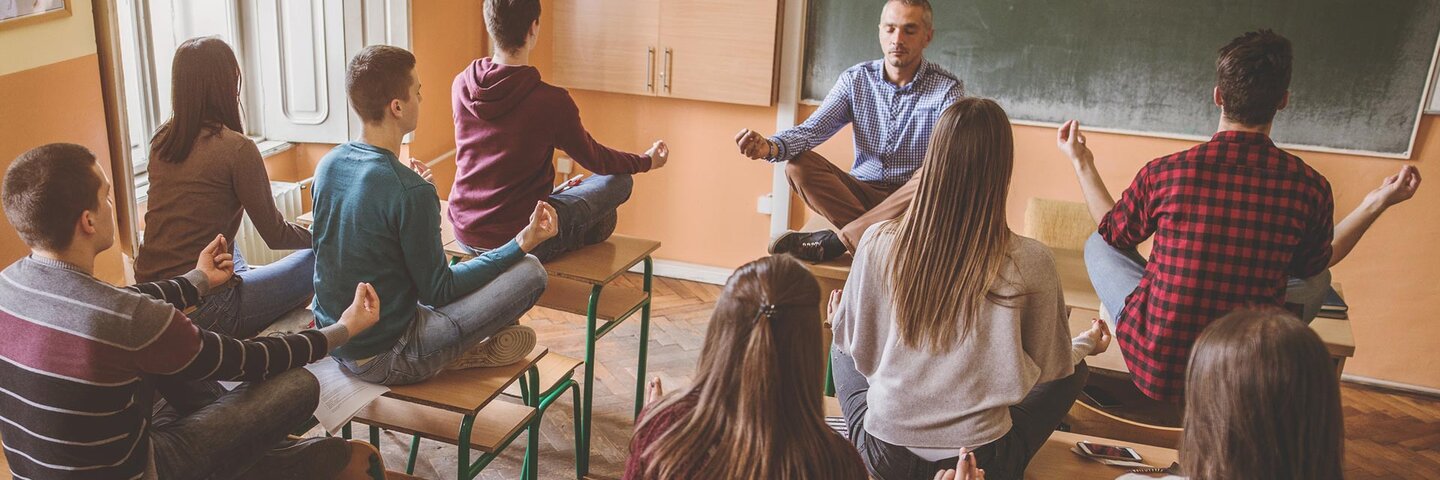 students meditating with teacher in classroom