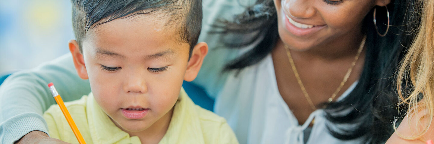 A teacher is helping a preschool students learn how to use his pencil.