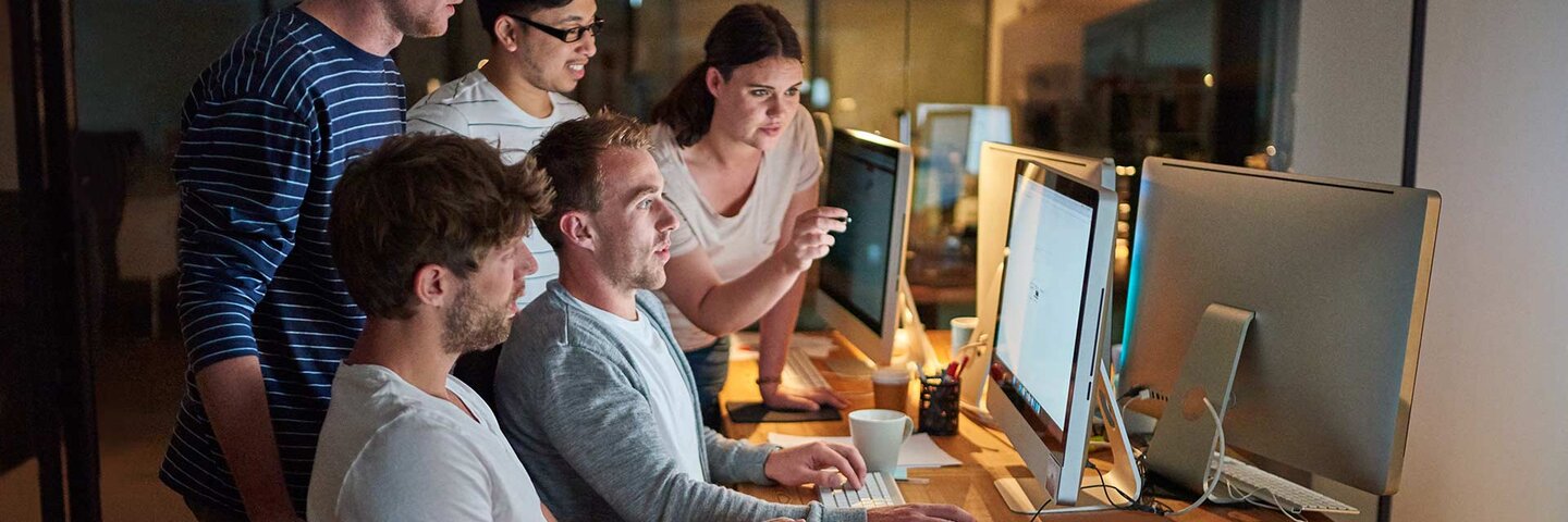 Shot of a group of young people using a computer together during a late night in a modern office