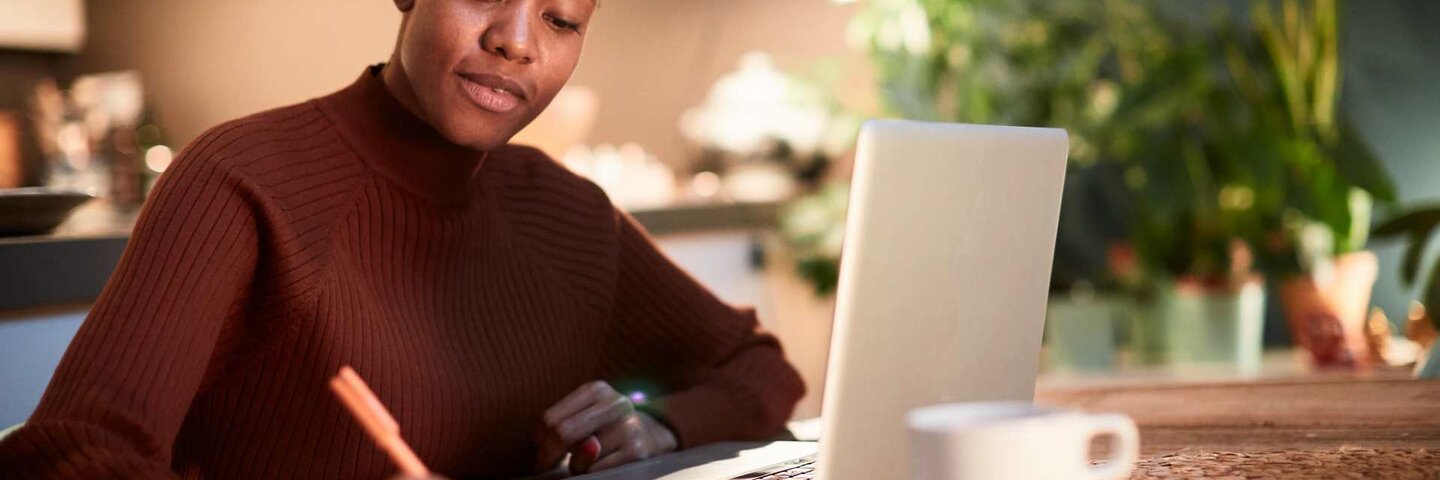Woman writing on notepad next to laptop.