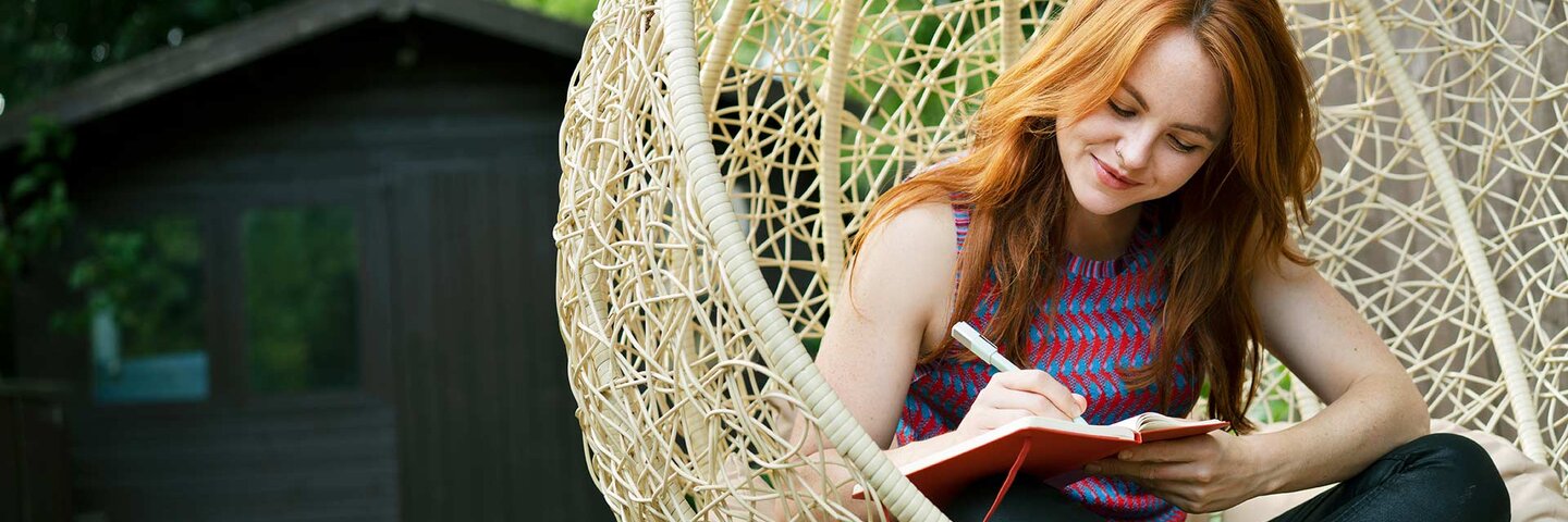 Woman writing in journal on swing seat outside